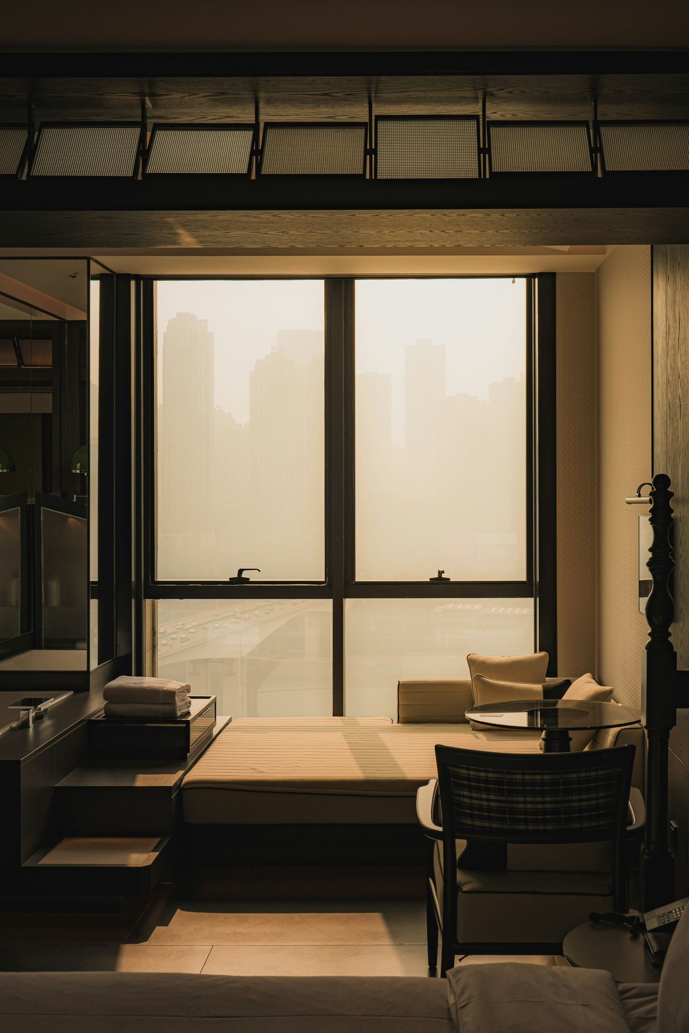 A hotel room window seat in warm afternoon light, a city skyline softened by haze beyond the glass